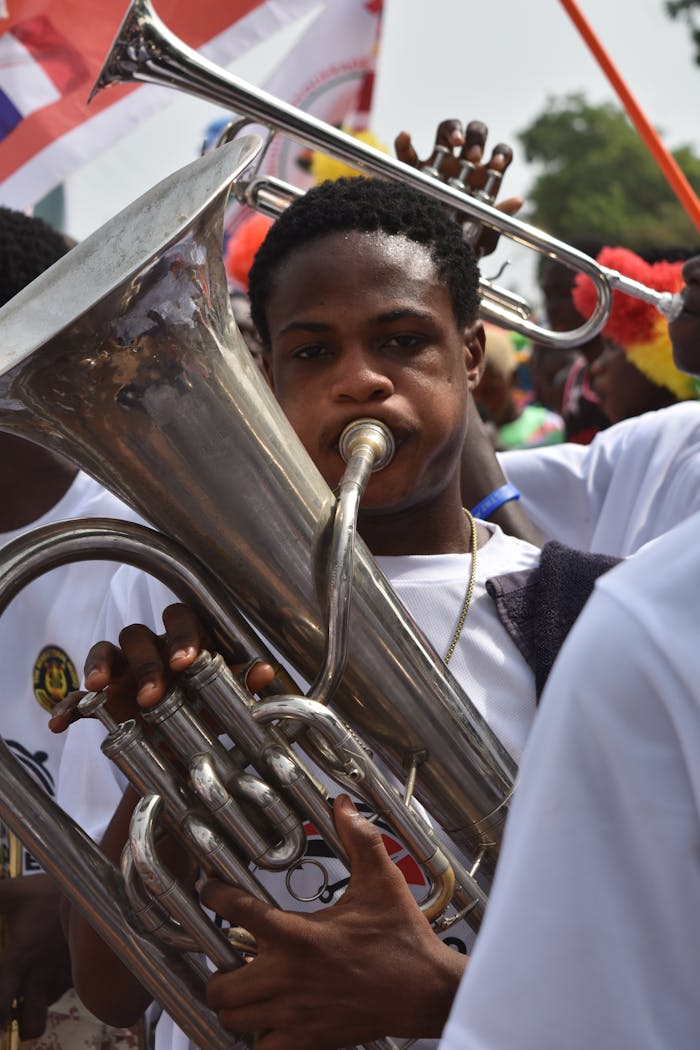 A young musician passionately plays the tuba during a lively outdoor parade, with flags waving in the background.