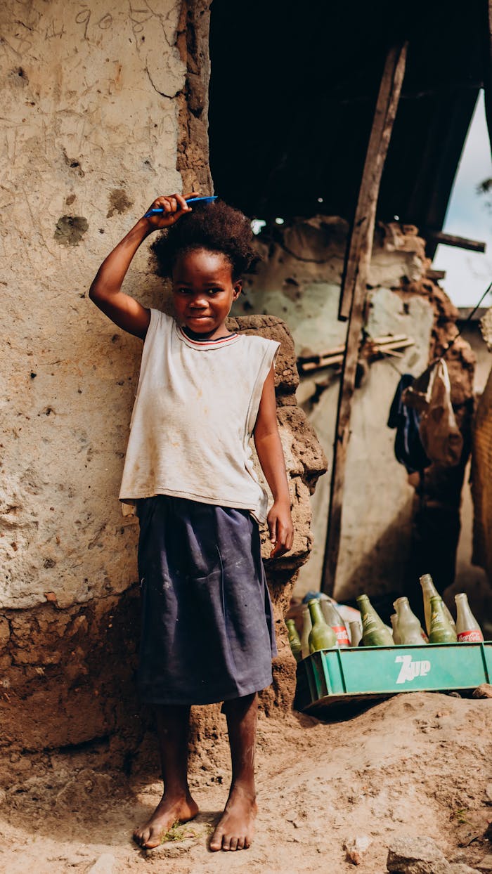 services-10 A young girl stands in a rural Nigerian setting, surrounded by rustic elements and holding a comb.