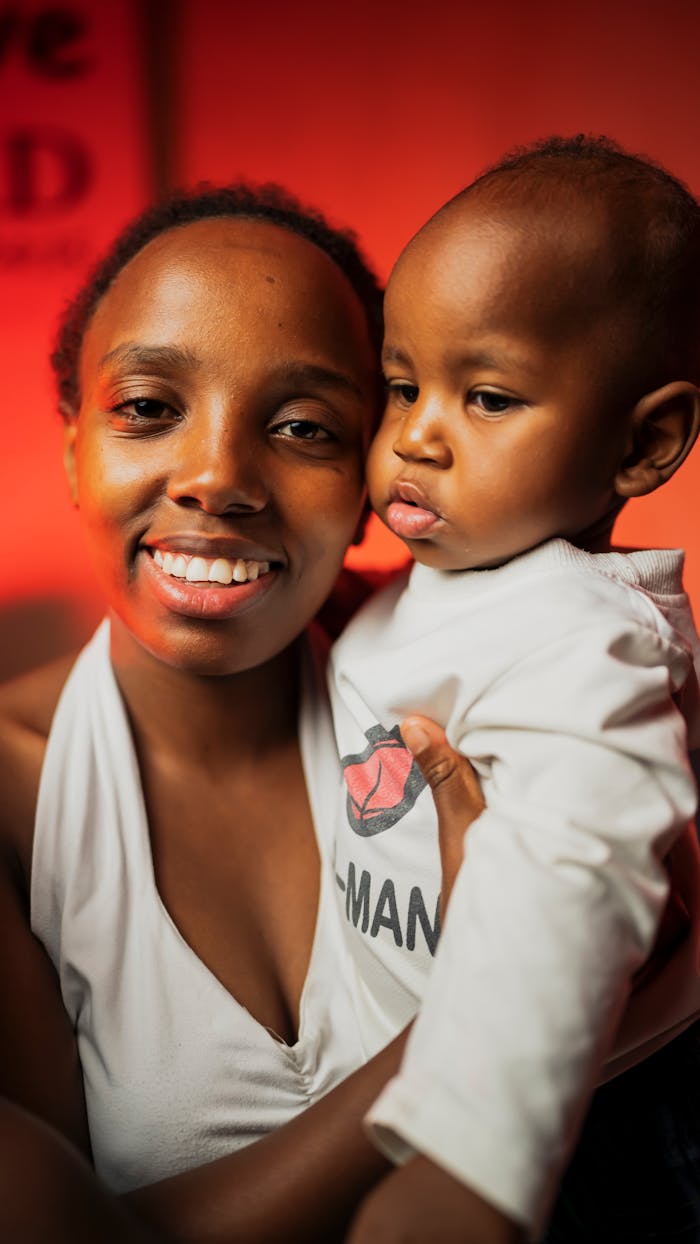 our-story-01 A cheerful African mother lovingly holds her baby against a warm, vibrant backdrop.